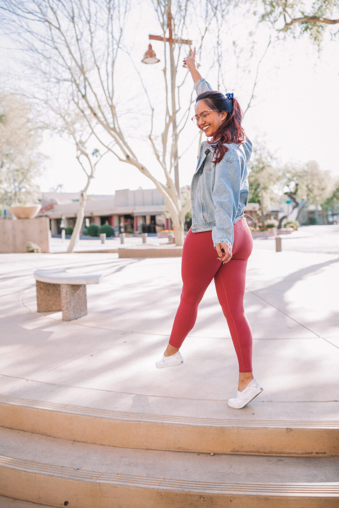 Woman wearing pink leggings and a denim jacket standing with her back to the camera holding her hand up with a peace sign