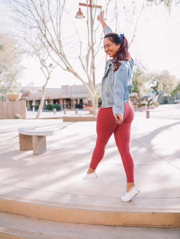 Woman wearing pink leggings and a denim jacket standing with her back to the camera holding her hand up with a peace sign