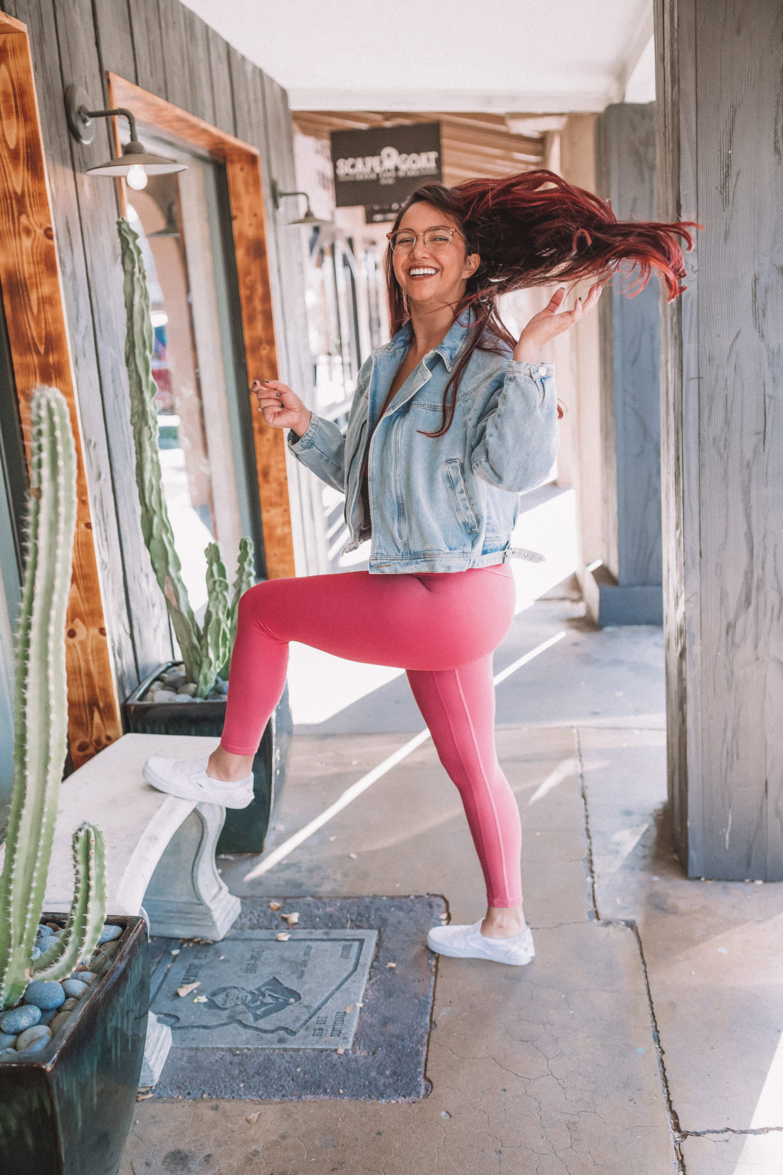 Woman wearing pink leggings and a denim jacket standing and flipping her hair