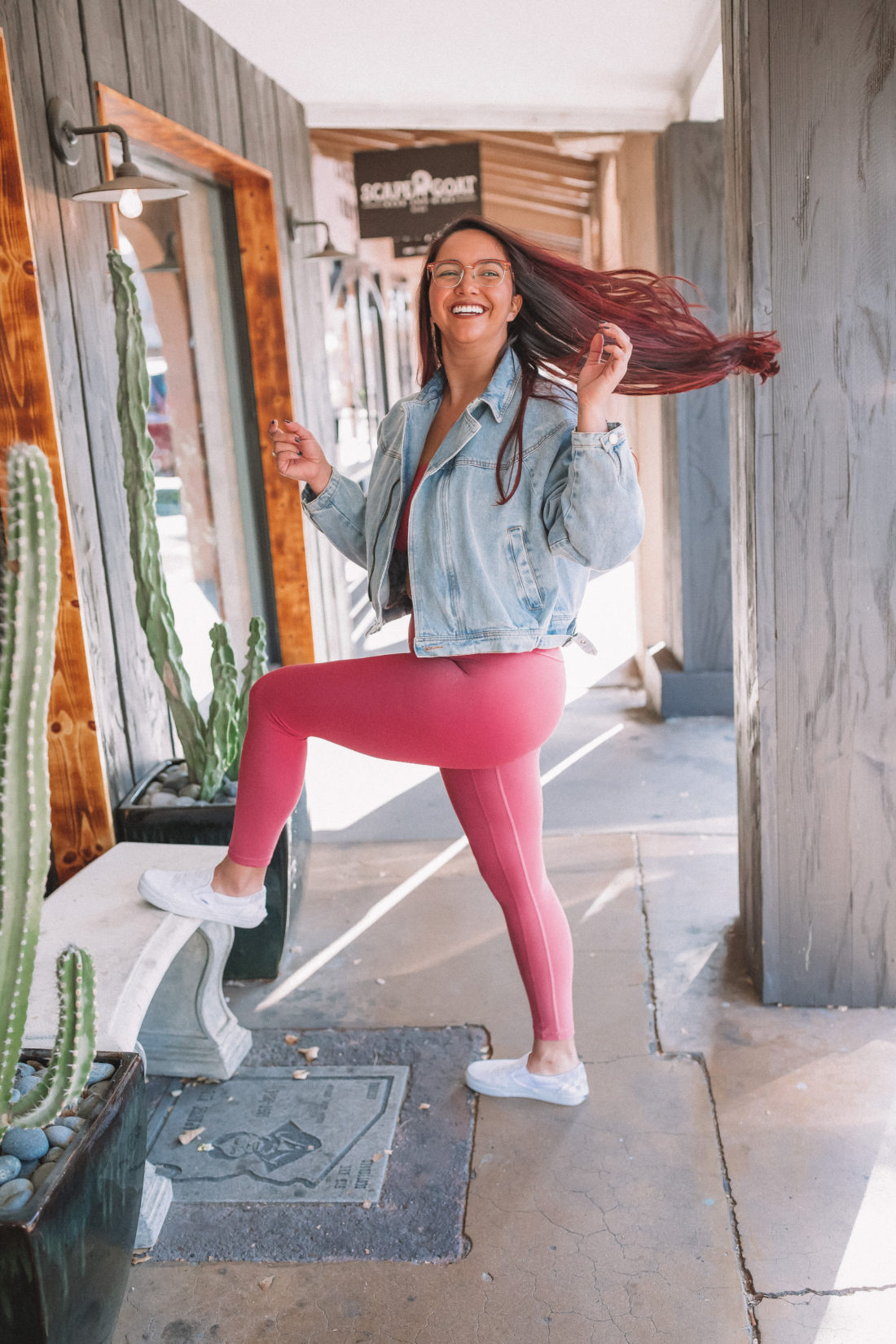 Woman wearing pink leggings and a denim jacket standing and flipping her hair